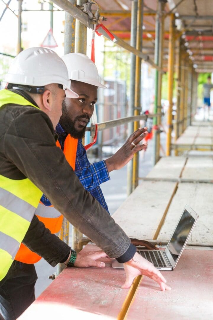 Two men in hard hats looking at a laptop.